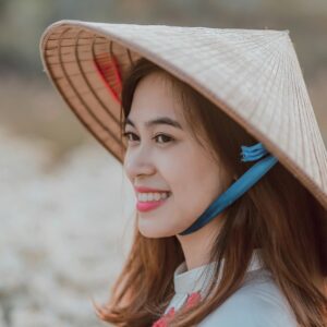 Young woman smiling in a Vietnamese hat, enjoying a sunny day outdoors.